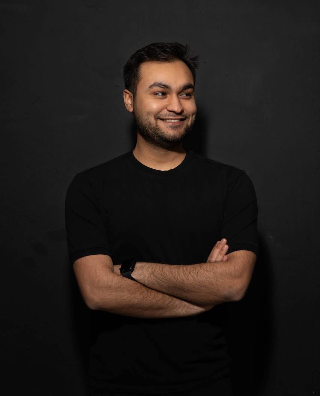 Portrait of Anand looking towards the right, smiling with his hands crossed